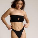 Woman wearing black strapless system against a neutral background