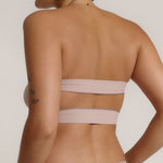 Woman wearing a beige strapless against a plain background