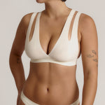 A person wearing a white, solid-colored bra and matching thong, with unique strap details and a v-neckline.