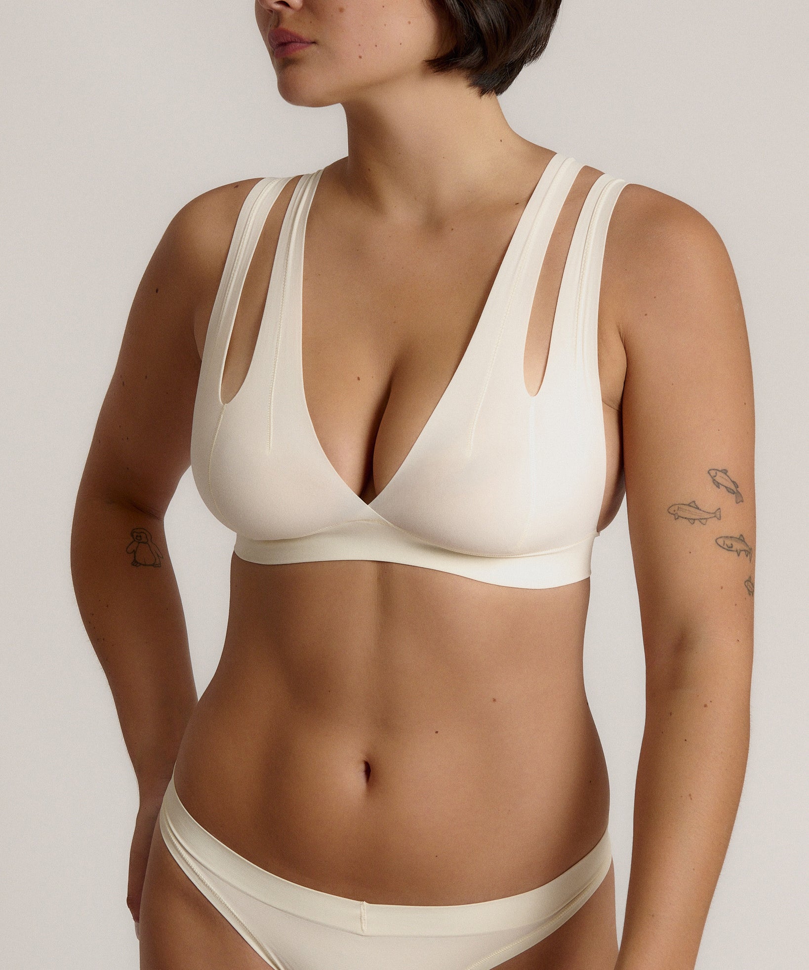 A person wearing a white, solid-colored bra and matching thong, with unique strap details and a v-neckline.