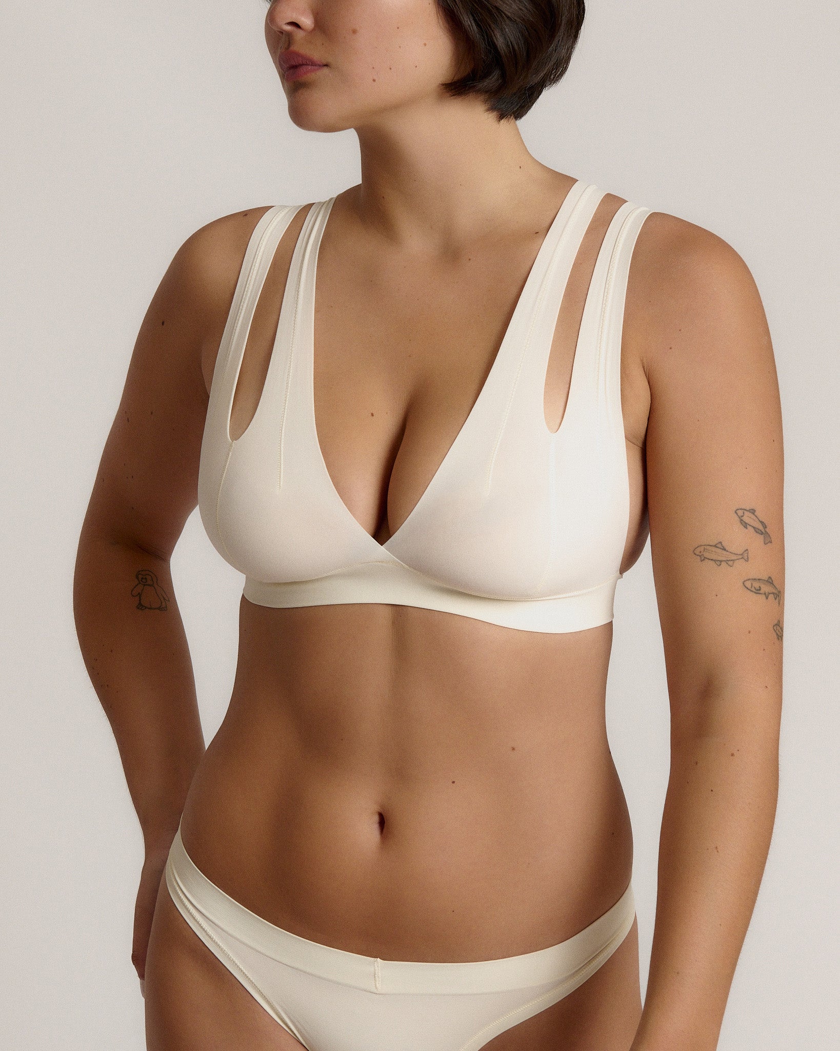 A person wearing a white, solid-colored bra and matching thong, with unique strap details and a v-neckline.