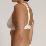 A person wearing a white, solid-colored bra and matching thong, with unique strap details and a v-neckline.