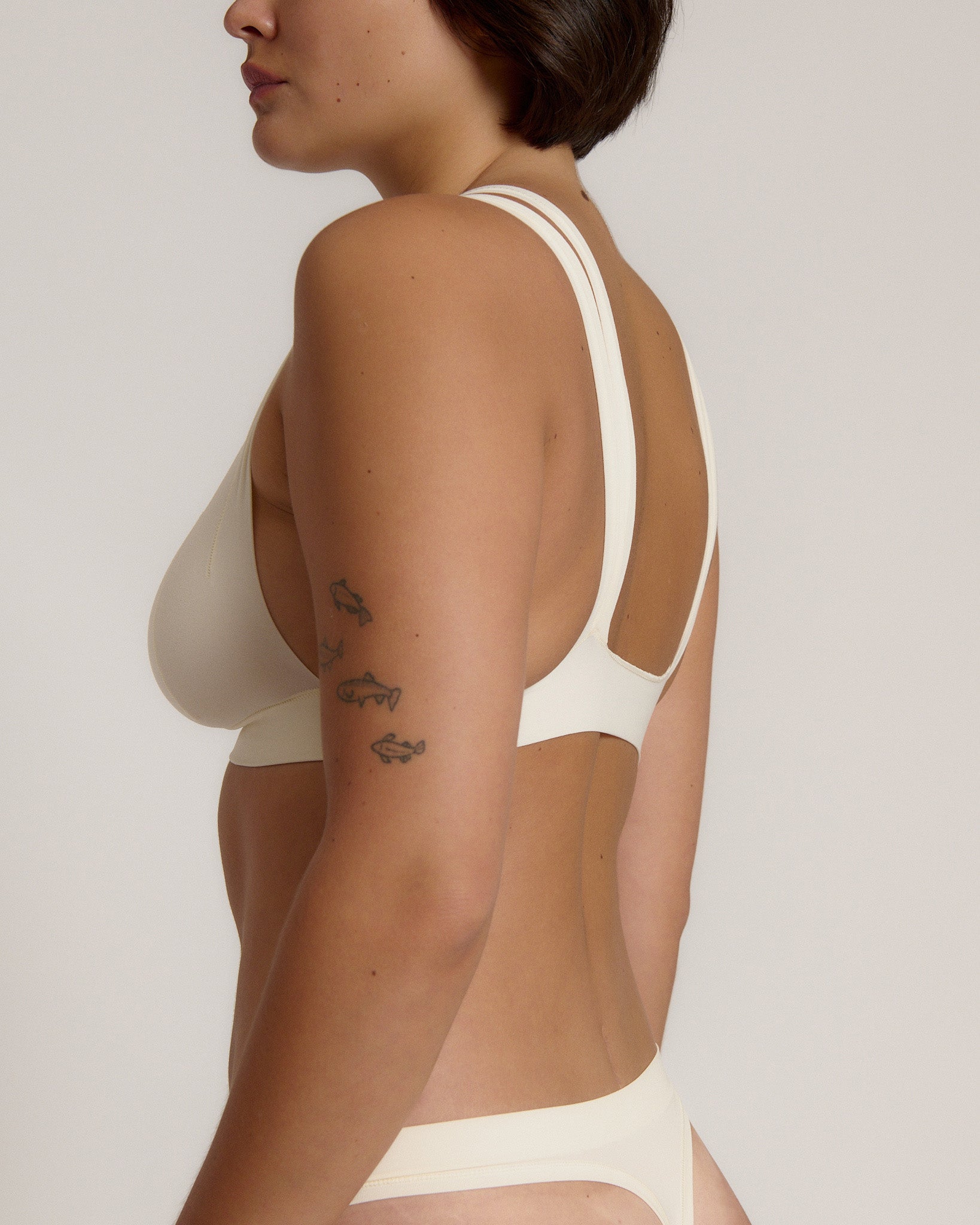 A person wearing a white, solid-colored bra and matching thong, with unique strap details and a v-neckline.