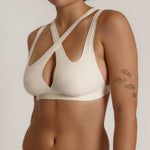 A person wearing a white, solid-colored bra and matching thong, with unique strap details and a v-neckline.