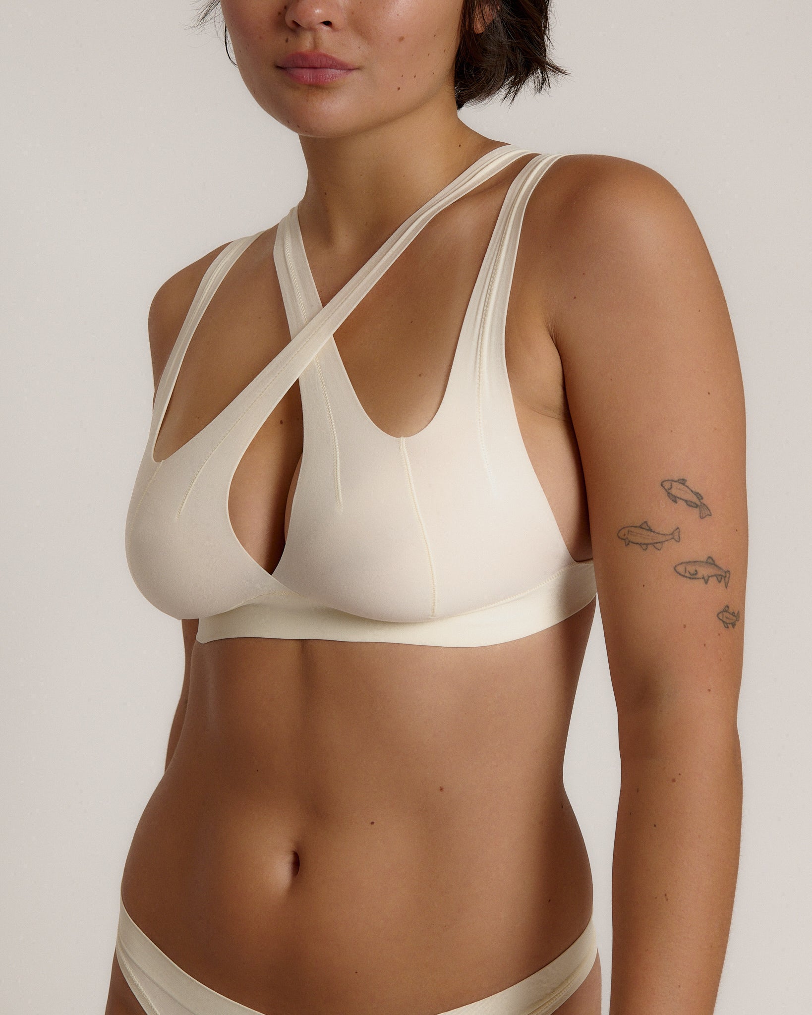 A person wearing a white, solid-colored bra and matching thong, with unique strap details and a v-neckline.