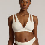 A person wearing a white, solid-colored bra and matching thong, with unique strap details and a v-neckline.