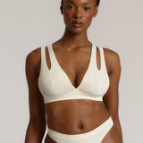 A person wearing a white, solid-colored bra and matching thong, with unique strap details and a v-neckline.