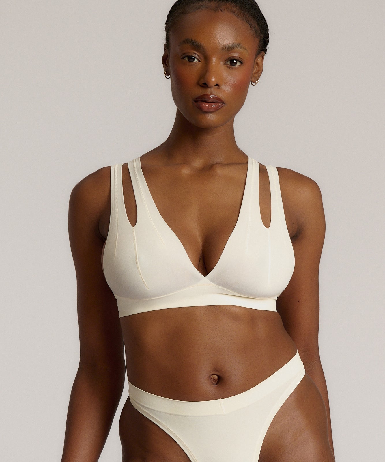 A person wearing a white, solid-colored bra and matching thong, with unique strap details and a v-neckline.