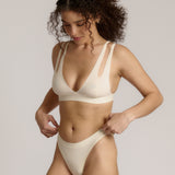 A person wearing a white, solid-colored bra and matching thong, with unique strap details and a v-neckline.
