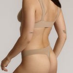 Woman wearing a light tee system and matching thong against a plain background.