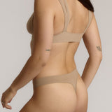 Woman wearing a light tee system and matching thong against a plain background.