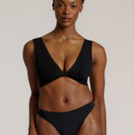 Woman wearing a black twist system and thong against a plain background