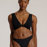 Woman wearing a black twist system and thong against a plain background