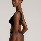 Woman wearing a black twist system and thong against a plain background
