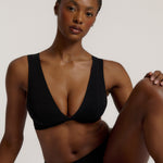 Woman wearing a black twist system and thong against a plain background