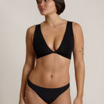 Woman wearing a black twist system and thong against a plain background