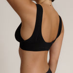Woman wearing a black twist system and thong against a plain background