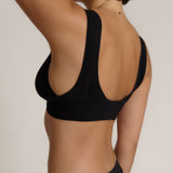 Woman wearing a black twist system and thong against a plain background