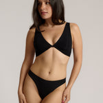 Woman wearing a black twist system and thong against a plain background