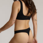 Woman wearing a black twist system and thong against a plain background