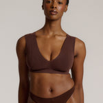 A woman wearing a brown Vii System bra, which is designed with a deep neckline, wide straps, and a smooth back.