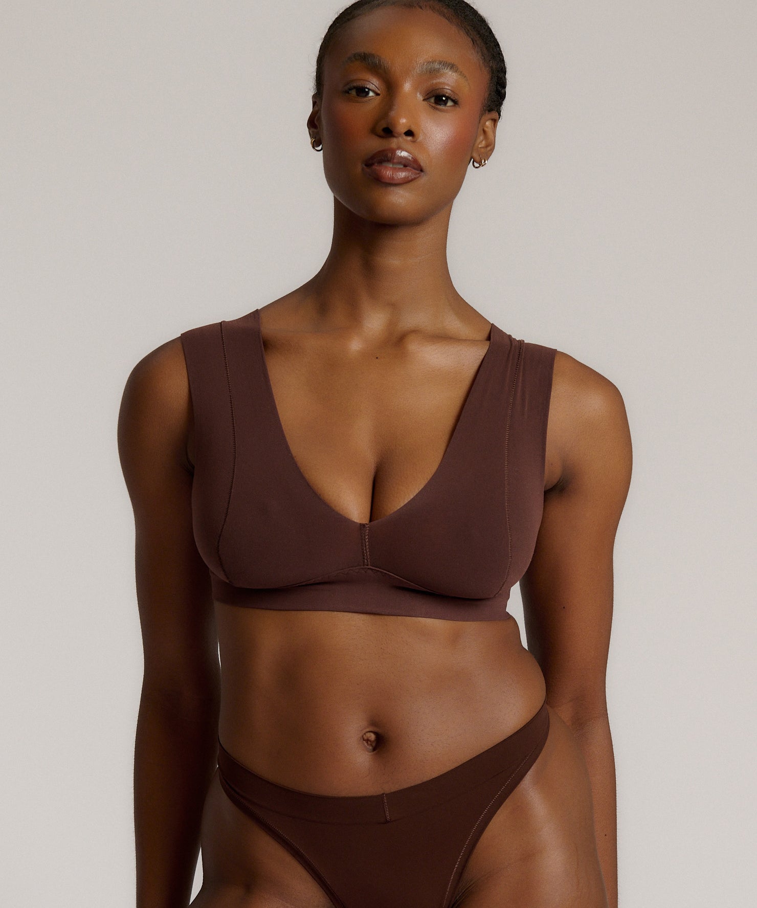 A woman wearing a brown Vii System bra, which is designed with a deep neckline, wide straps, and a smooth back.