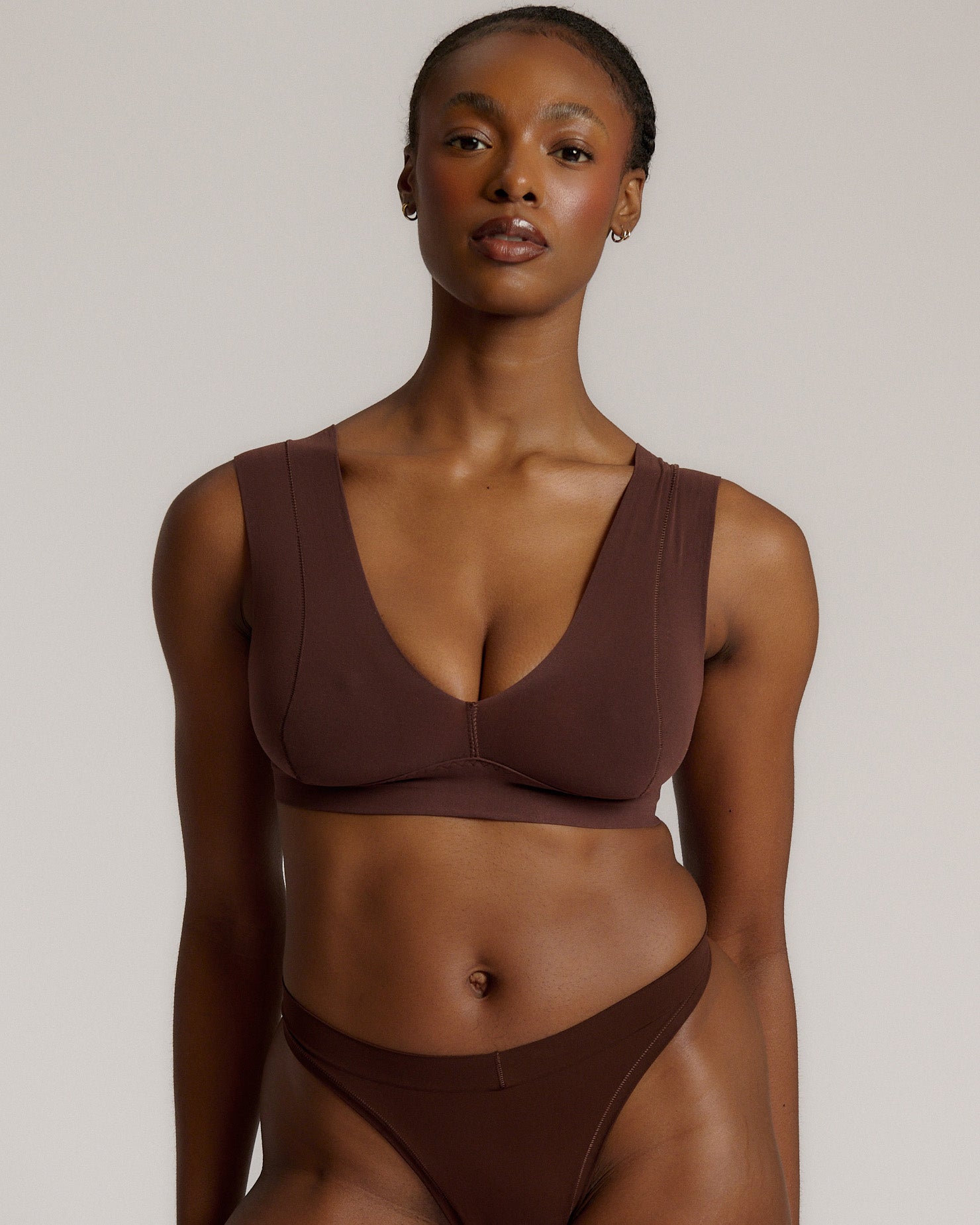 A woman wearing a brown Vii System bra, which is designed with a deep neckline, wide straps, and a smooth back.