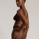 A woman wearing a brown Vii System bra, which is designed with a deep neckline, wide straps, and a smooth back.