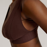 A woman wearing a brown Vii System bra, which is designed with a deep neckline, wide straps, and a smooth back.