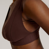A woman wearing a brown Vii System bra, which is designed with a deep neckline, wide straps, and a smooth back.