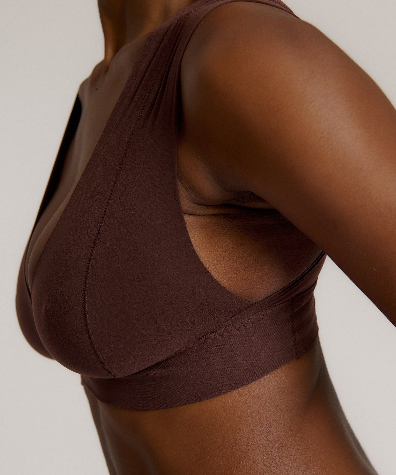 A woman wearing a brown Vii System bra, which is designed with a deep neckline, wide straps, and a smooth back.