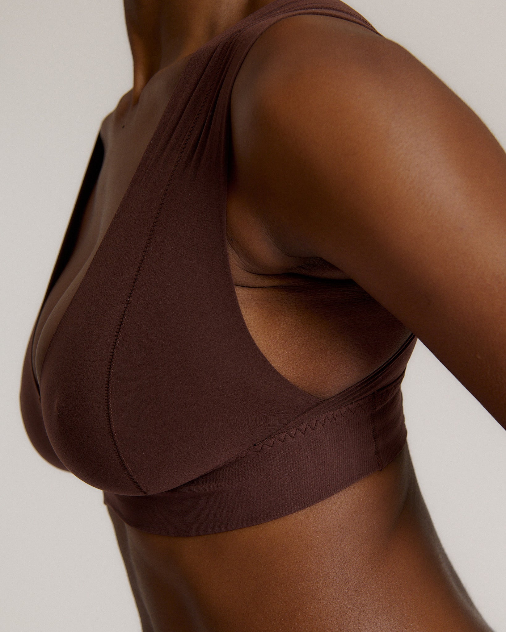 A woman wearing a brown Vii System bra, which is designed with a deep neckline, wide straps, and a smooth back.