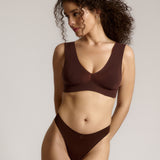 A woman wearing a brown Vii System bra, which is designed with a deep neckline, wide straps, and a smooth back.