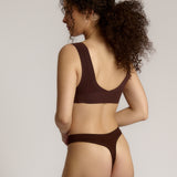 A woman wearing a brown Vii System bra, which is designed with a deep neckline, wide straps, and a smooth back.