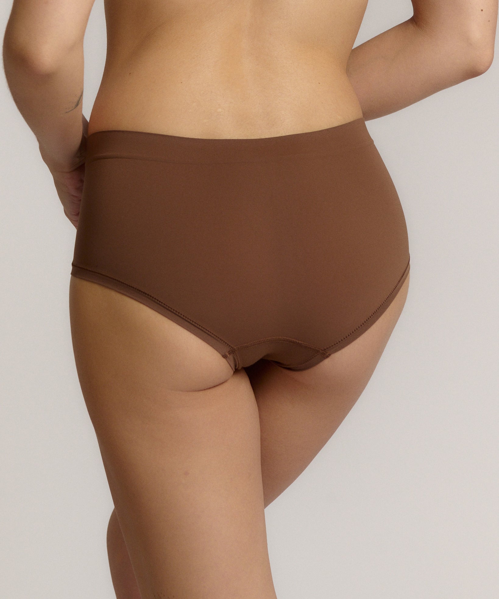 A mid-rise brown brief underwear with a seamless design, showing the waistband and part of the leg openings.