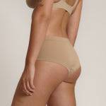 A person wearing a beige mid-rise brief with no visible lines, made from a stretchy fabric, showcasing the design's comfort and fit.