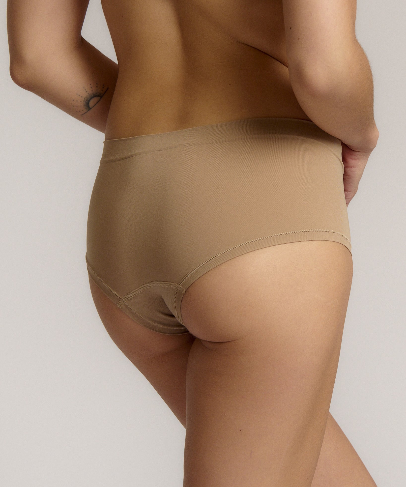 A person wearing a beige mid-rise brief with no visible lines, made from a stretchy fabric, showcasing the design's comfort and fit.