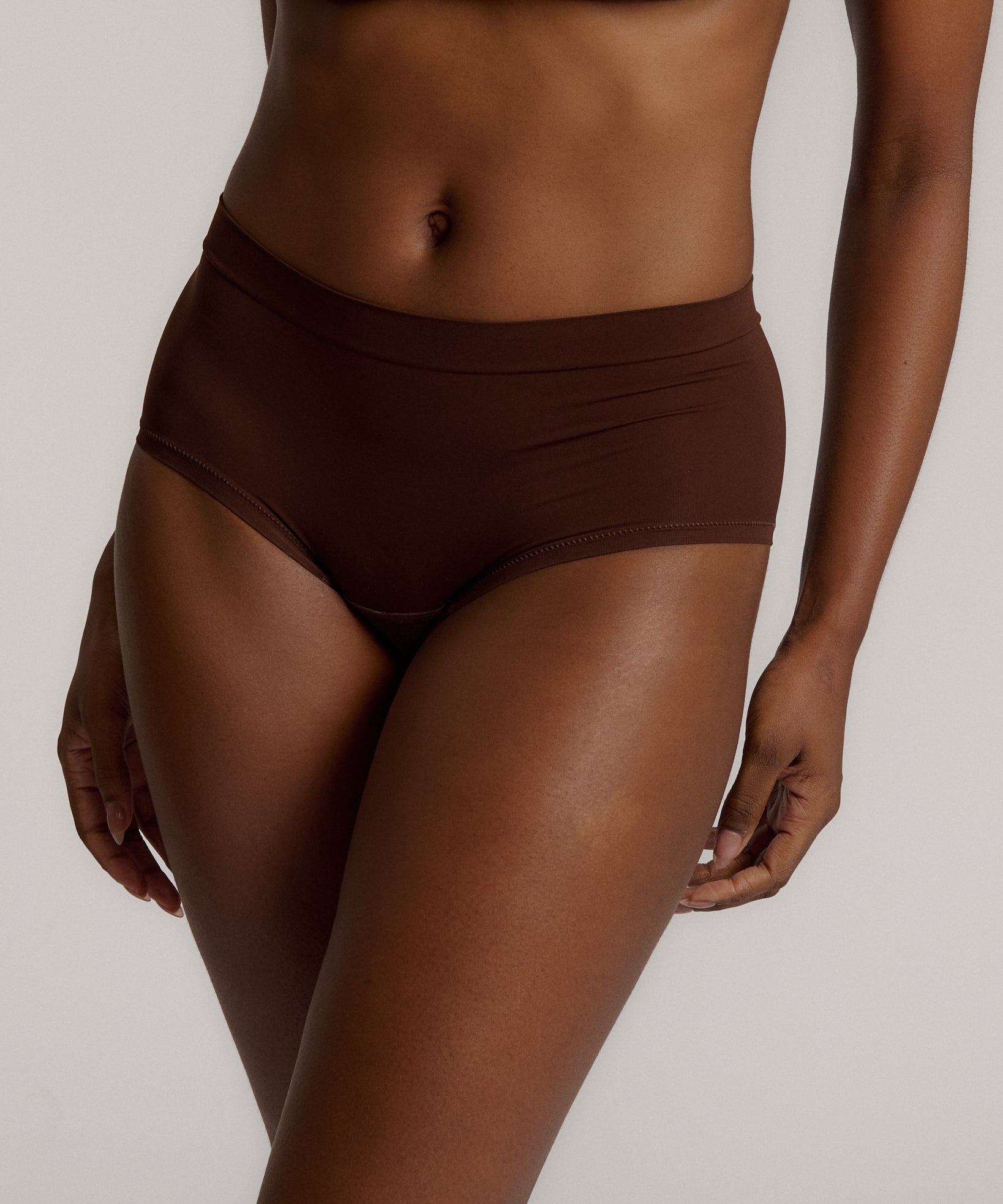 A person wearing a brown mid-rise brief underwear, showing the side profile of the underwear with no visible lines.