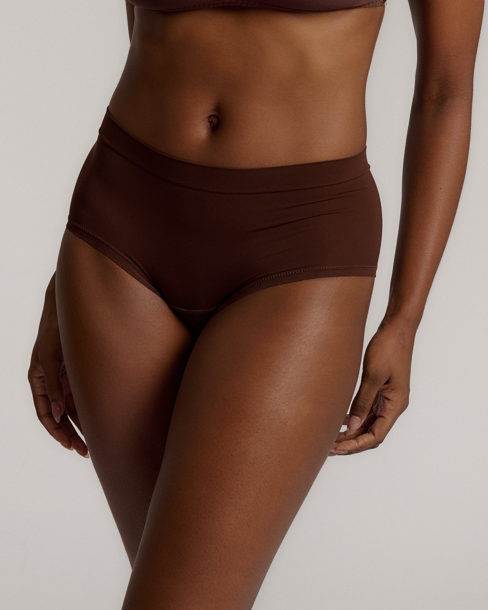 A person wearing a brown mid-rise brief underwear, showing the side profile of the underwear with no visible lines.
