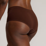 A person wearing a brown mid-rise brief underwear, showing the side profile of the underwear with no visible lines.
