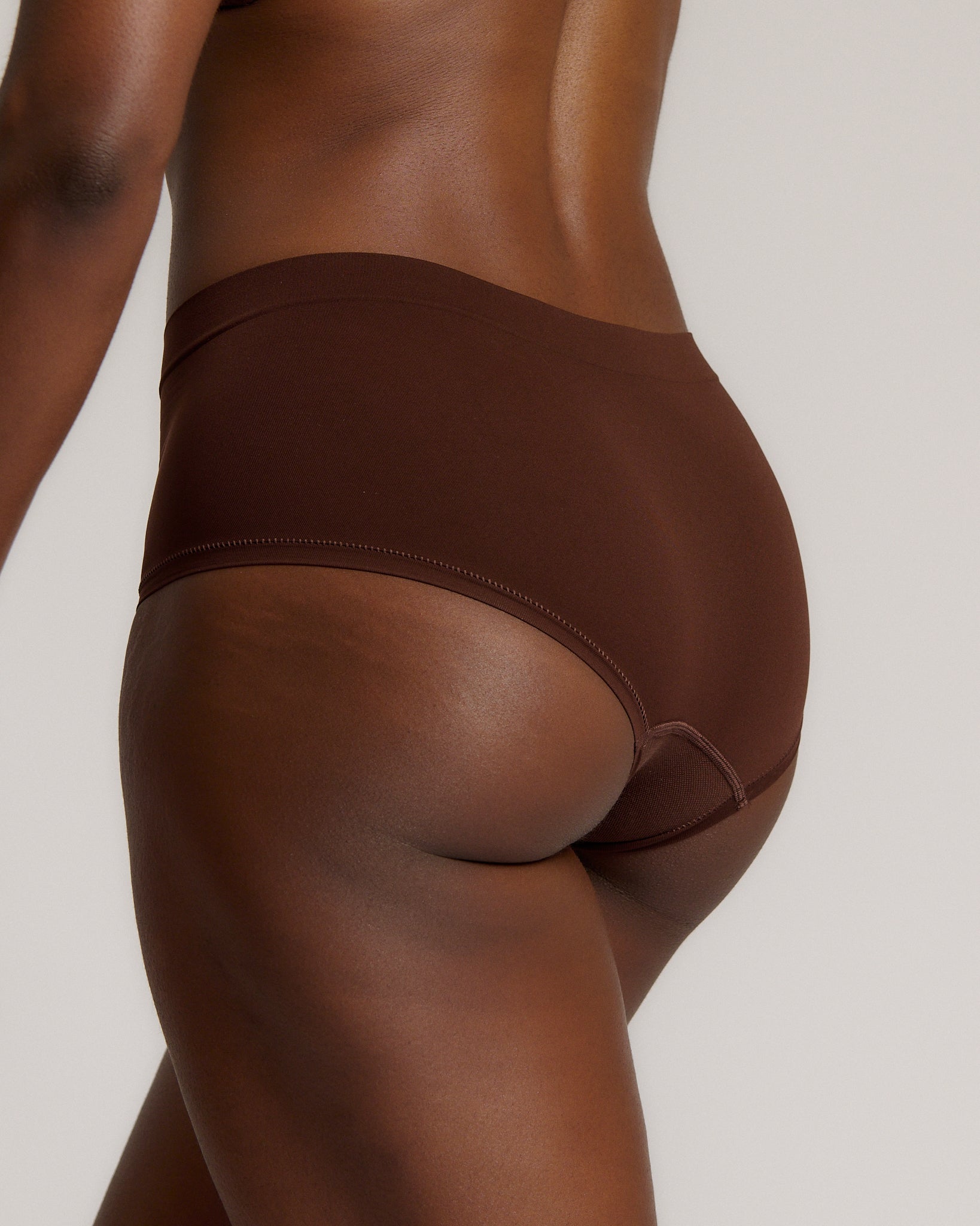 A person wearing a brown mid-rise brief underwear, showing the side profile of the underwear with no visible lines.