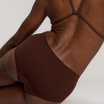 A person wearing a brown mid-rise brief underwear, showing the side profile of the underwear with no visible lines.