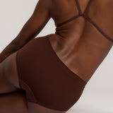 A person wearing a brown mid-rise brief underwear, showing the side profile of the underwear with no visible lines.