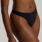 A woman wearing black thong underwear designed with a mid-rise cut.