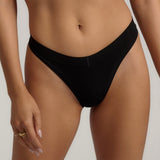 A woman wearing black thong underwear designed with a mid-rise cut.