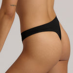 A woman wearing black thong underwear designed with a mid-rise cut.