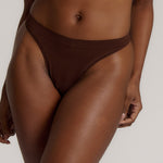 A woman wearing a brown thong on a plain background