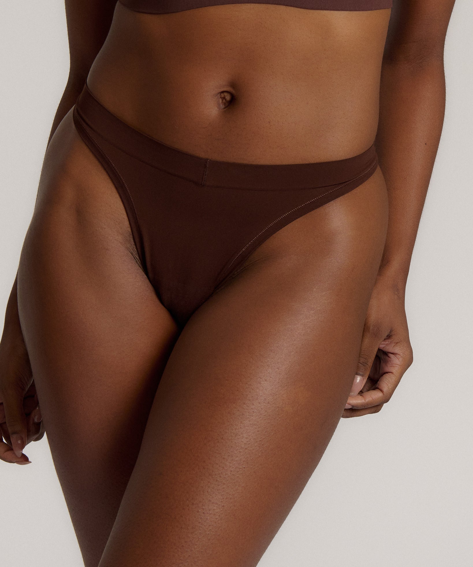 A woman wearing a brown thong on a plain background