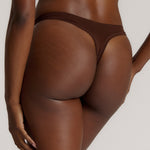 A woman wearing a brown thong on a plain background