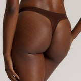 A woman wearing a brown thong on a plain background